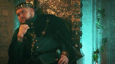 warlike medieval courageous strong man sits on old bronze throne, image tyrannical king. Carnival vintage costume velvet