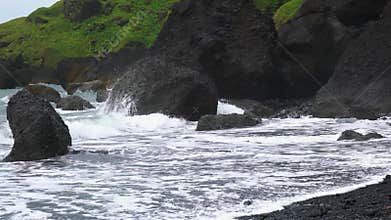 View of sea waves crash against black rocks.