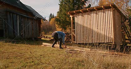 Person working on constructing a wooden structure outdoors near a log cabin. DIY home improvement and rustic living