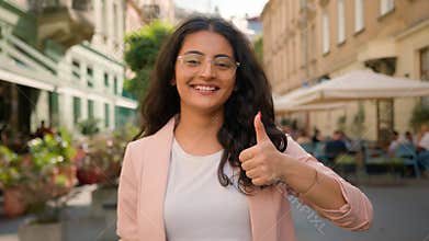 Charming cheerful young Indian Arabian ethnic woman girl female businesswoman positive showing thumb up outside city