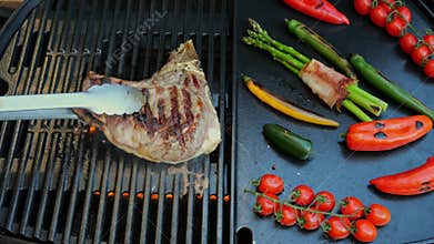 Beef T-Bone steak grill turn over on barbecue, grilled vegetables.