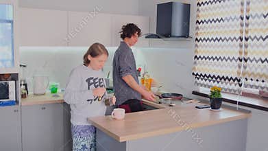 Caucasian Siblings Cooking Together At Stove Top, Sharing Utensils And Stirring Pans, Patterned Curtains And Modern Hood In