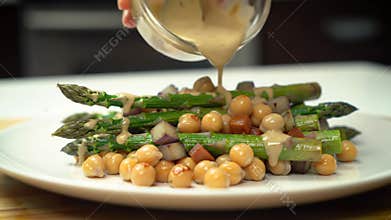 Pouring sauce over a healthy plate of asparagus, chickpeas and chopped potatoes. A delicious vegan meal with fresh seasonal