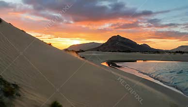 Breathtaking sunset over sand dunes and tranquil waters creating a serene desert landscape