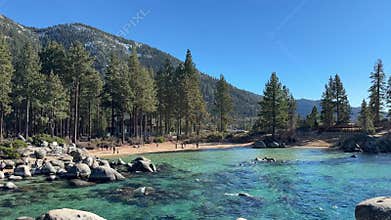 Wide scenic view of Sand Harbor beach cove with emerald water and pine forest background