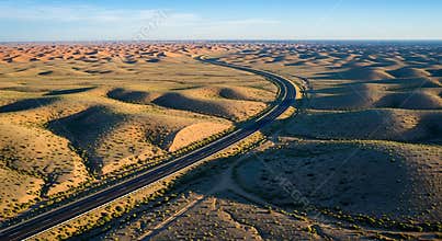 Aerial View of Asphalt Highway Winding Through Rolling Arid Desert Landscape at Sunrise