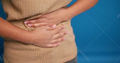 Sick woman holding belly, having stomach pain, diarrhea selective focus on hands on blue background
