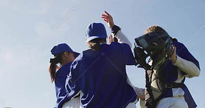 High-fiving female baseball players wearing blue jerseys and caps on sunny field, with catcher gear