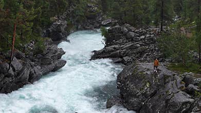 Adventurer stands near foaming rapids, capturing the raw power of nature in a Norwegian gorge