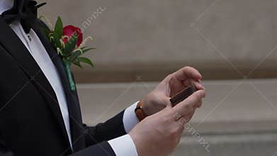 Groom Reading Vows On Phone Closeup Hands Holding Screen With Boutonniere In Formal Tuxedo