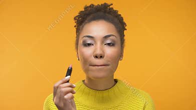 Pretty African-American girl applying lipstick and winking, ready for date