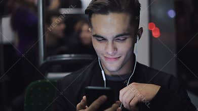 Portrait of young headsome men in headphones listening to music and browsing on mobile phone in public transport. City