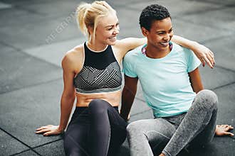 Two fit young women laughing together on a gym floor
