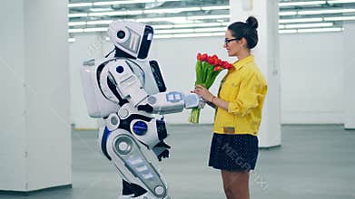 A droid gives red tulips to a girl and she hugs it.