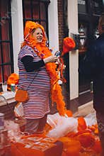 Portrait of woman dressed in orange, crazy hat, selling junk on King`s Day festivity
