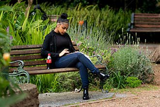 Young woman sitting on park bench using a tablet or phone before Covid