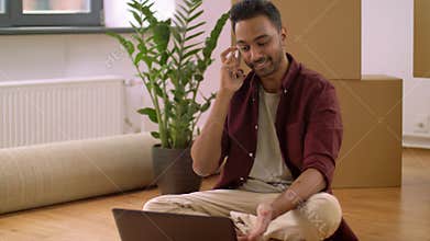 Man with laptop and boxes calling on phone at home