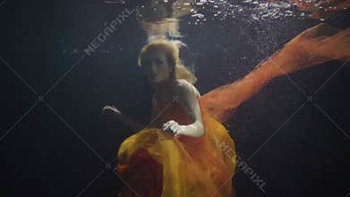 Mysterious woman swimming like mermaid under water in on dark background