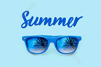 Summer textured blue text and blue sunglasses with palm trees reflections isolated in a light blue background