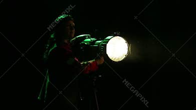 A young woman illuminator directs a beam of light from a spotlight.