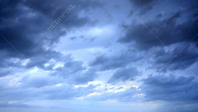 Dramatic Storm Clouds Over Moody Blue Sky With Rolling Dark Layers And Distant Light