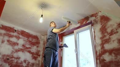 Construction worker plastering ceiling with taping knife