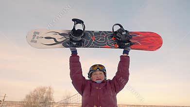 Cheerful older woman rising up snowboard on snowy slope at winter resort