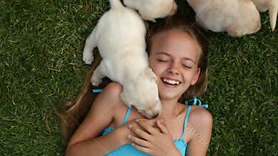 Girl lying in the grass with by her labrador puppy dogs