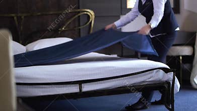 Hotel cleaner makes a double bed in a small, cozy hotel room. Slow motion.