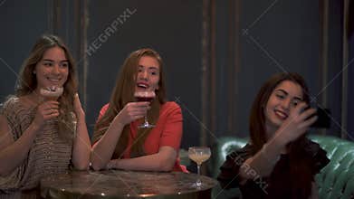 Three cute girls sit in a cafe or restaurant beautifully posing and taking a photo selfie for social networks