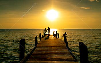 Happy family play together on summer vacation at wooden bridge at sunset. Parent and children playing at the beach on holiday.