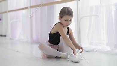 Cute ballet dancer tying ballet shoes before training