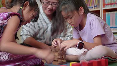 Young mother and her daughters try to build wooden block tower.
