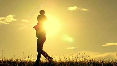 Silhouette of father and son walking on sunset background. Dad is holding his son on his shoulders. The concept of a
