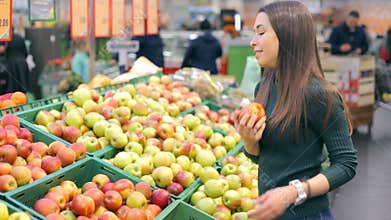 Woman selecting fresh red apples in grocery store produce department
