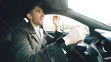 Happy handsome businessman driving car and singing. Man is happy after making deals and drives home