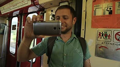Male tourist smiling and taking video of amusing scene on train with cellphone