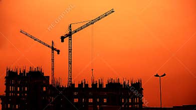 Cranes near building block of flats, sunset time