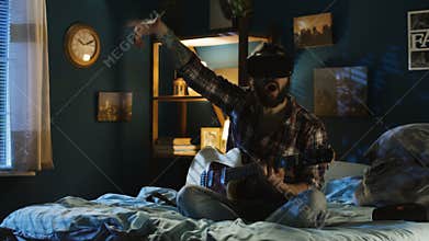 Man playing guitar in VR glasses on bed at night