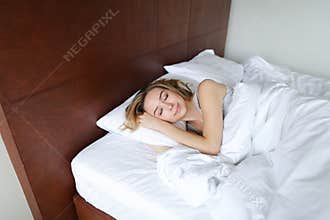Young female person sleeping in morning on wooden bed with white linens.