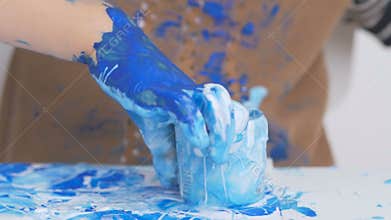 A little girl stained her hands and clothes in paint while drawing. The child carefully examines the dirty hands.