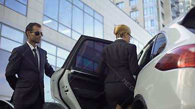 Personal driver meeting and opening car door for lady boss, bodyguard duties