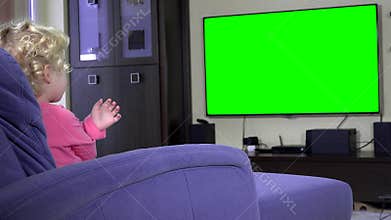 Addicted little girl point finger and wave looking tv. Green chroma key screen