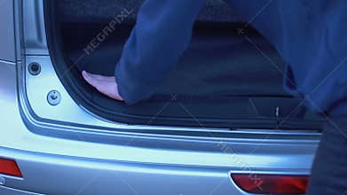 Man hiding forbidden packets in car trunk, drugs smuggling, illegal trading