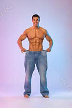 Young man showing how much weight he lost with big jeans. Fat to fit concept. Fitness poster