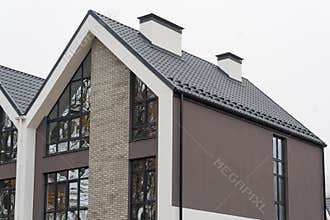 Newly installed construction frame house rain gutter system and chimney pipe on the metal roof top. Big panoramic windows.