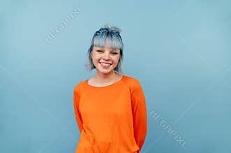 Smiling hipster girl with colored hair stands on a blue background with a happy face and looks at the camera.Smiling hipster girl