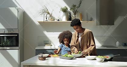 Happy Black mom show preteen girl how to cook salad