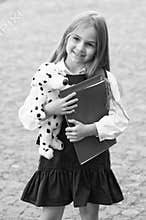 Adding fun to study. Happy child hold toy dog and books outdoors. Back to school supplies. Fashion uniform. Formal dress
