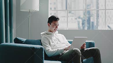 Joyful student in hoodie reads home assignment on tablet